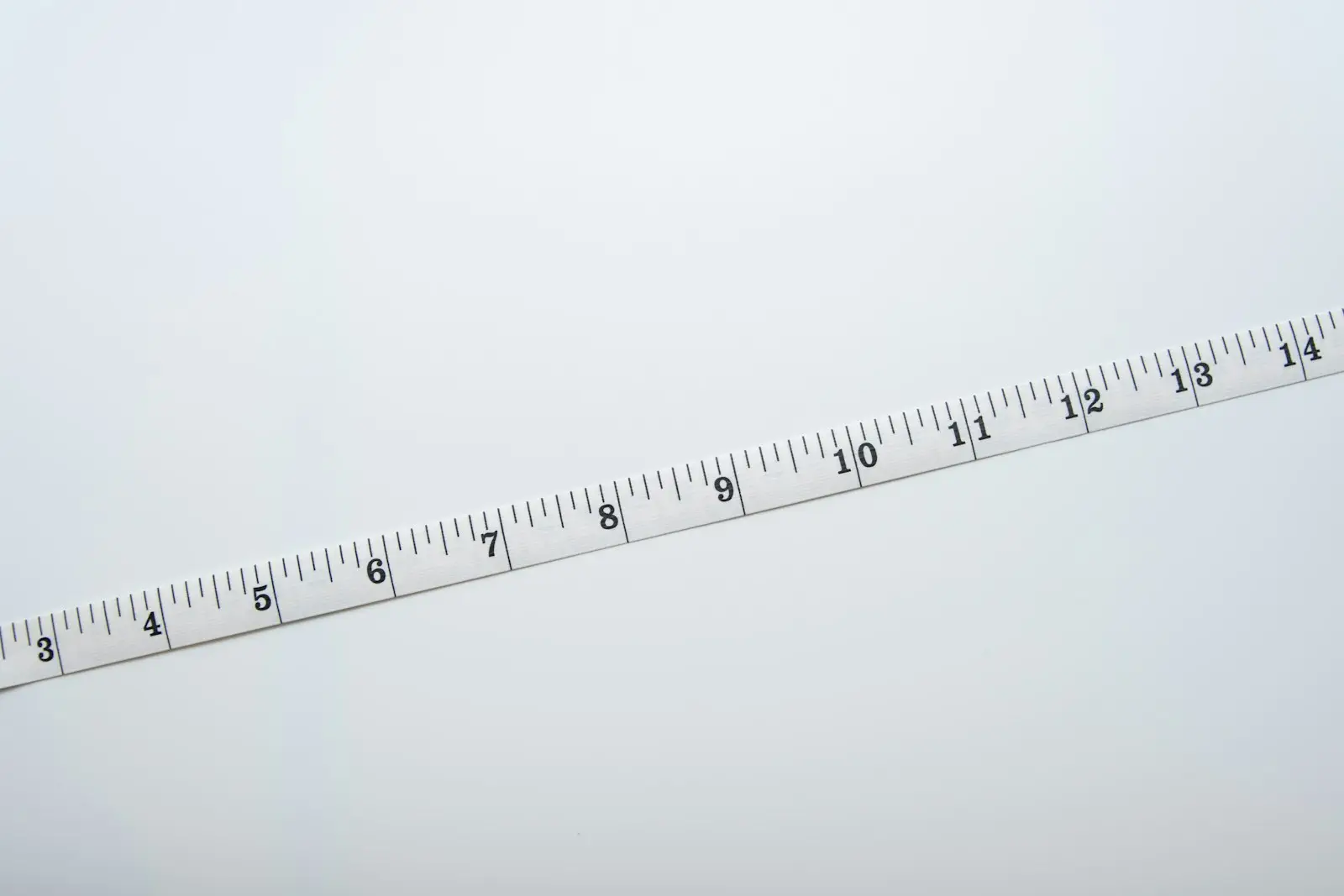 A white tape measure with inch markings on a pale background