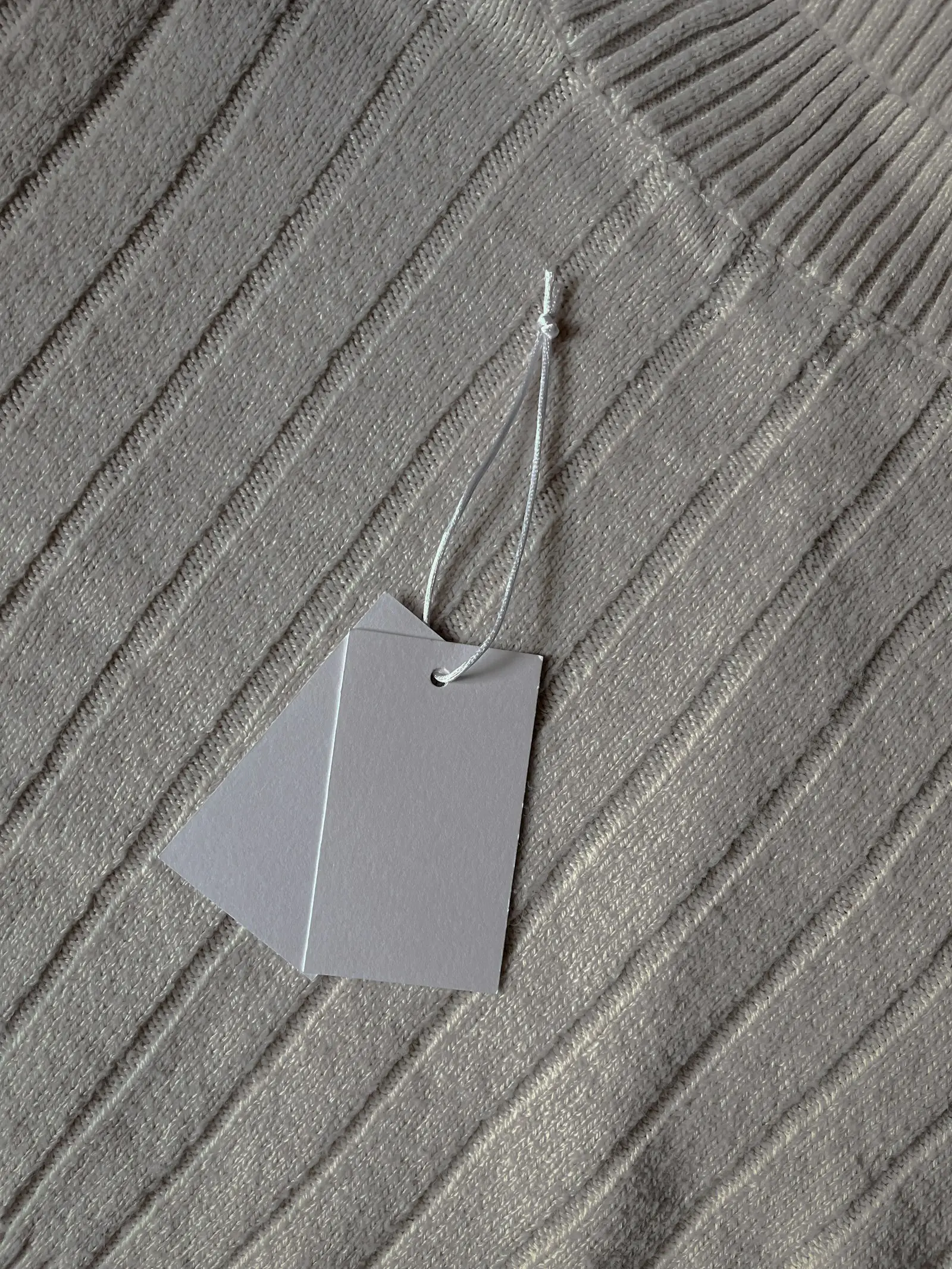 A blank swing tag hanging from a string against textured fabric
